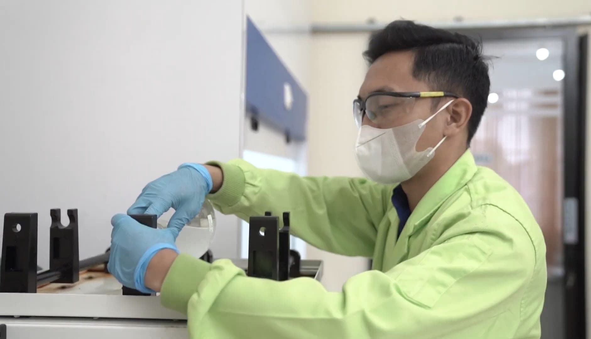 Analis berkacamata pelindung dan masker memasang labu kaca pada dudukan instrumen.