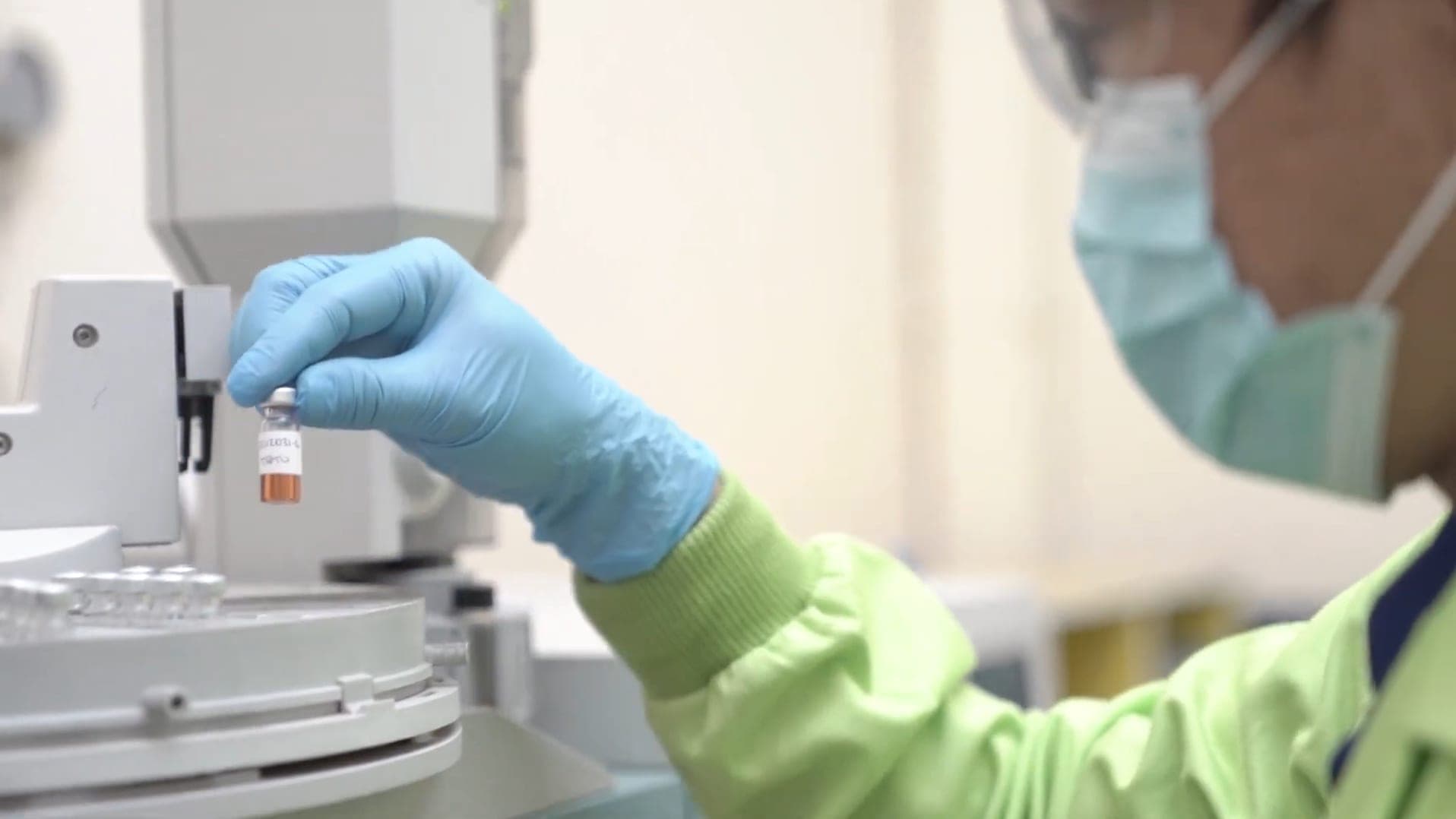 Analis bersarung tangan memasang vial sampel pada autosampler instrumen.